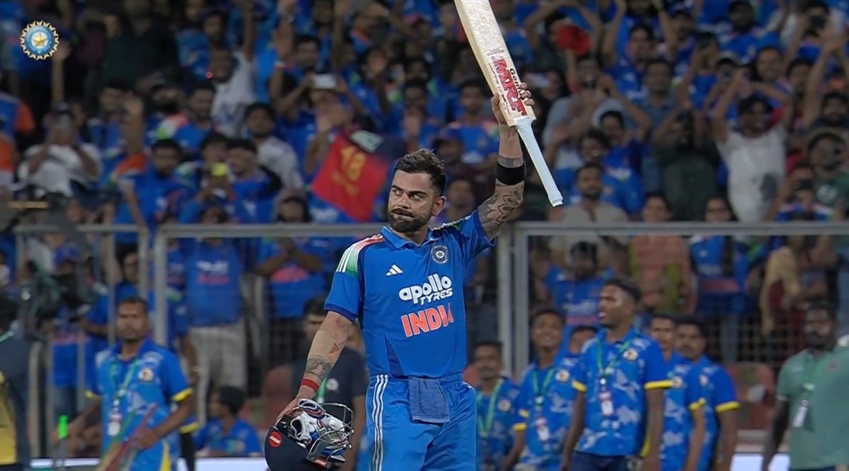 Virat Kohli in India blue raising his bat, with a cheering crowd behind him